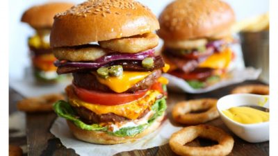 A huge burger with onion rings on the side.